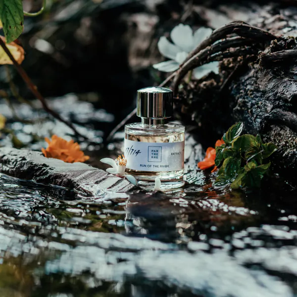 Parterre Fragrances perfume bottle labeled 'Run of the River' resting in a forest stream with flowers and moss