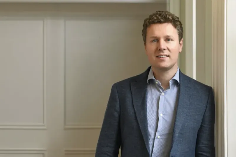 Dr Jonathan Dunne, Consultant Plastic and Reconstructive Surgeon, smiling in a navy suit and light blue shirt