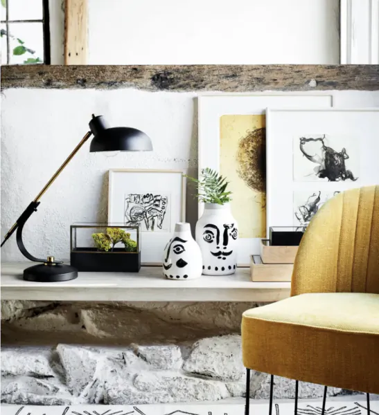 Modern home office desk with black lamp, face vases, framed art, and yellow chair against white brick wall