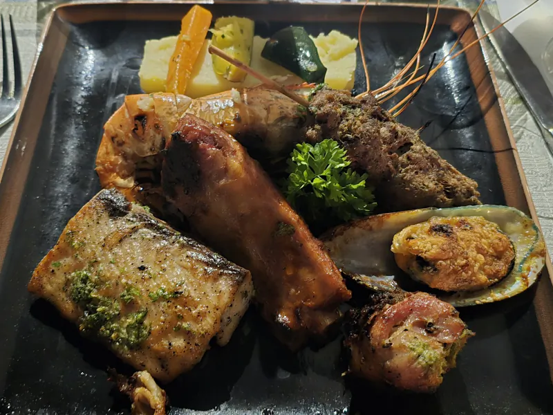 Grilled seafood platter with fish, shrimp, bacon-wrapped scallop, stuffed clam, vegetables and parsley garnish on black plate