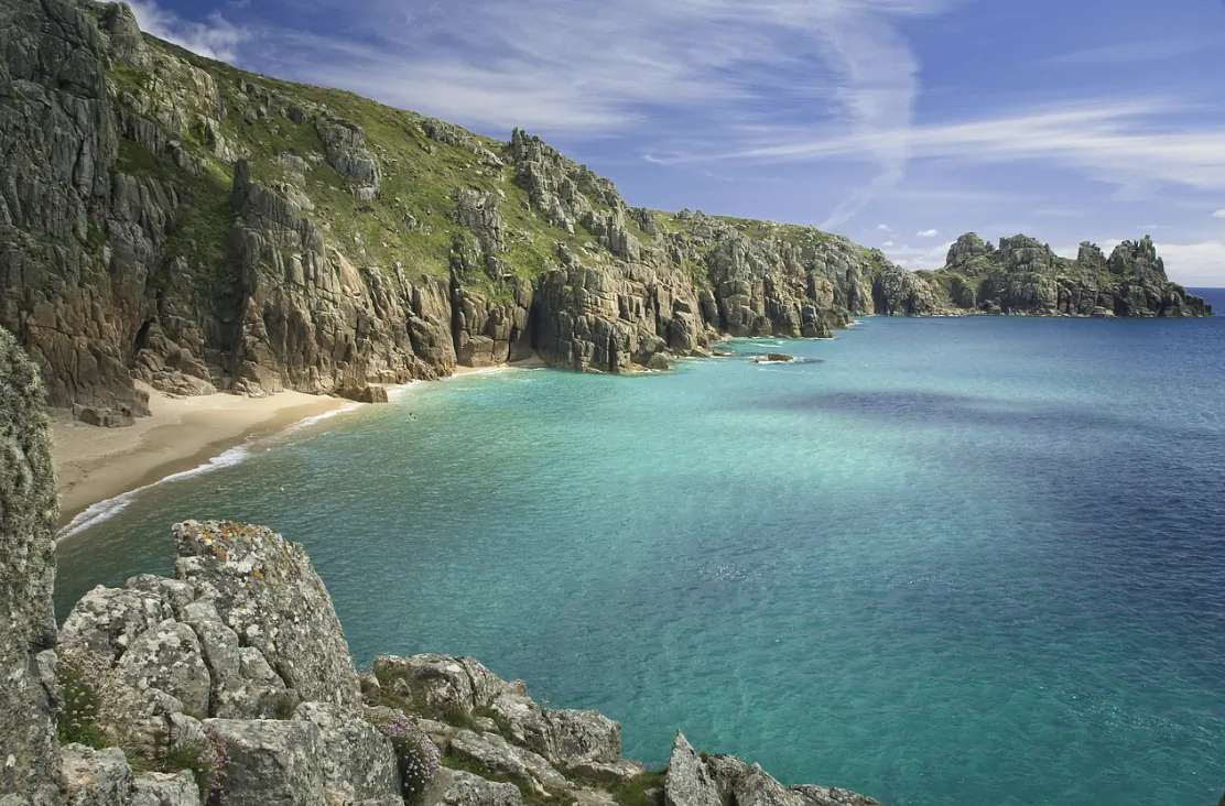 Turquoise sea meets rugged cliffs and a small sandy cove under a bright blue sky