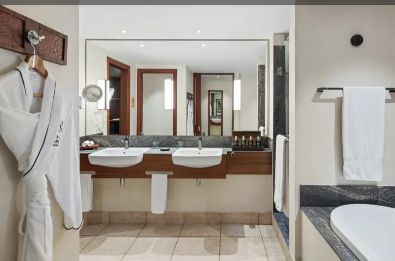 Luxury hotel bathroom with two white robes hanging, double sinks, large mirror, and bathtub