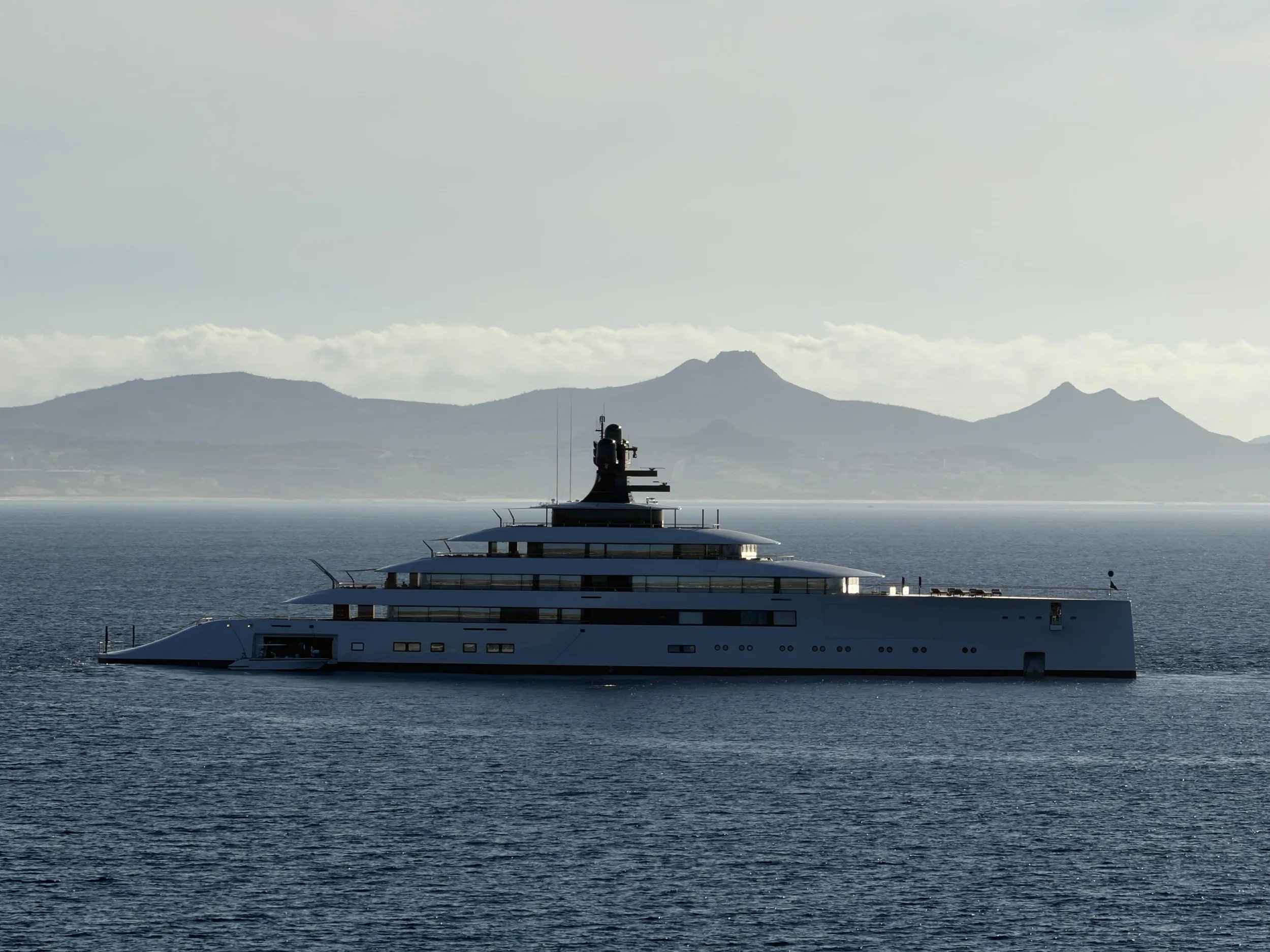 Large white luxury yacht sailing on calm sea with misty mountains in background