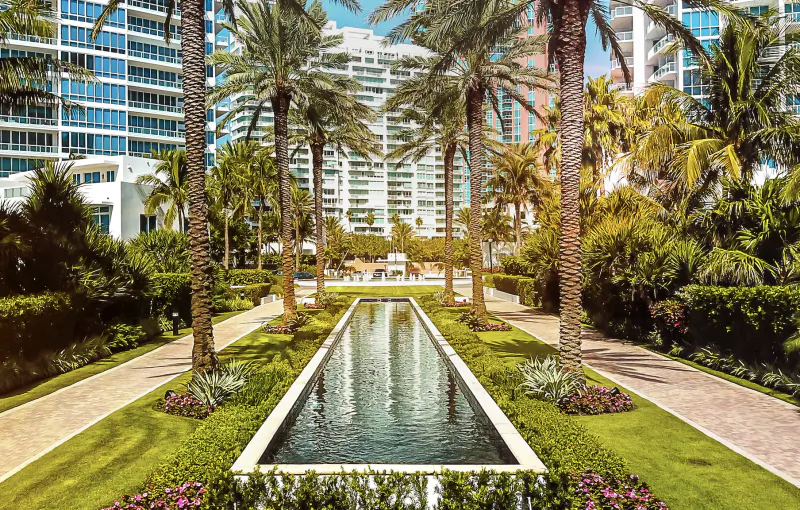 Long rectangular reflecting pool lined with palm trees and lush landscaping, modern high-rise luxury residences in the background