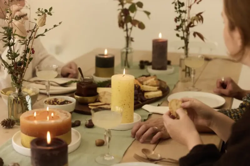 Friends gathered around a candlelit dinner table with cheese, crackers, and festive St Eval candles
