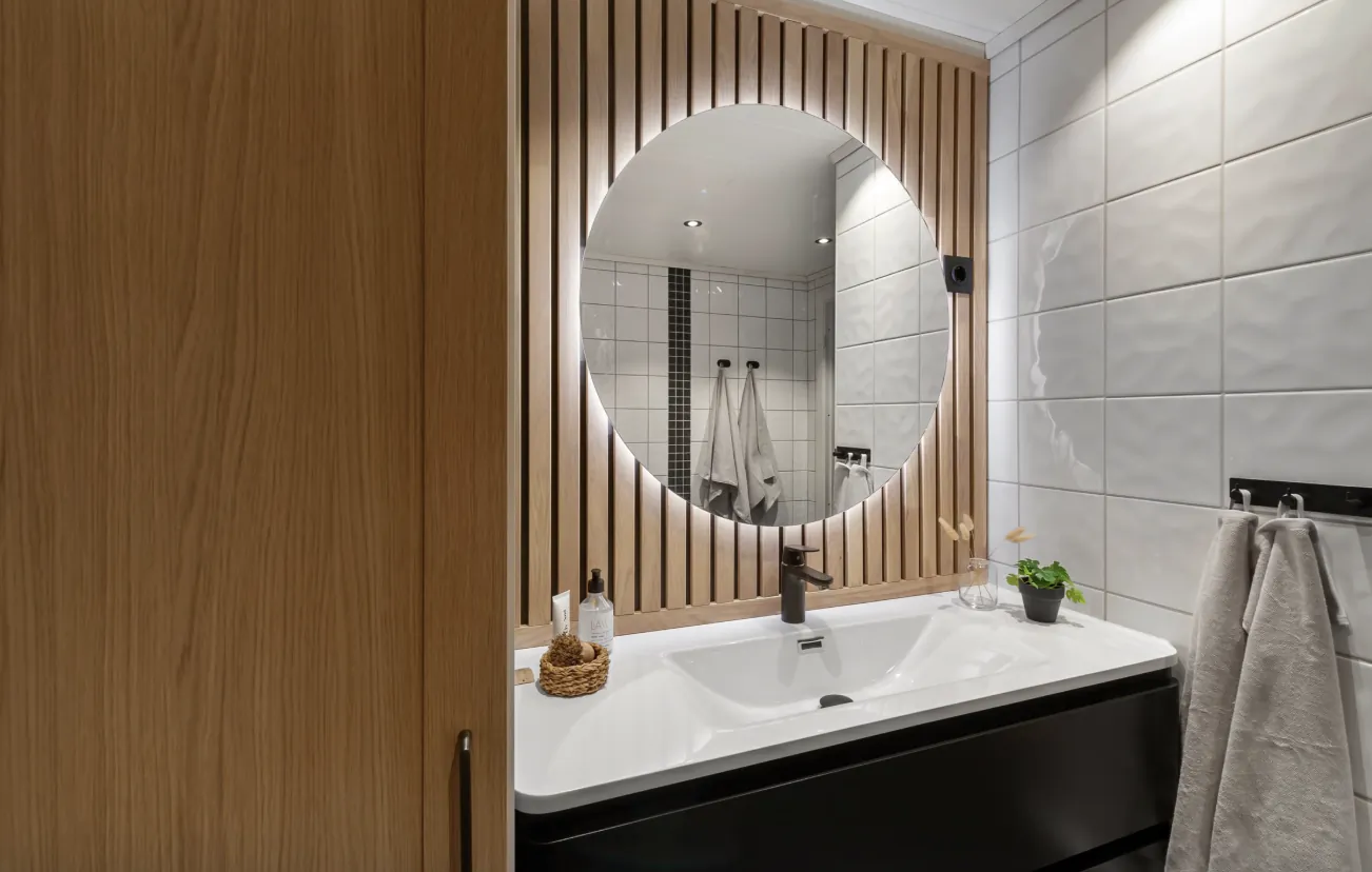 Modern bathroom vanity with round LED backlit mirror, white sink, black faucet, and wood slat accent wall