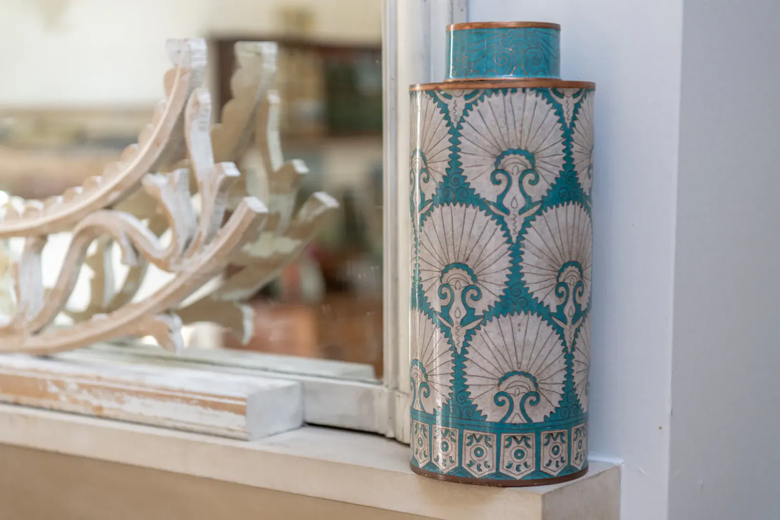 Decorative turquoise and cream cloisonne vase with fan and scroll pattern on a windowsill