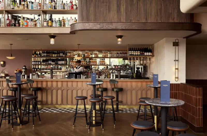 Modern bar interior with wooden counter, high stools, and shelves of liquor bottles at Coppa Club London Bridge
