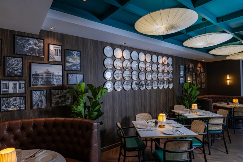 Modern restaurant interior with teal ceiling, wooden walls, framed photos, decorative plates, and set dining tables