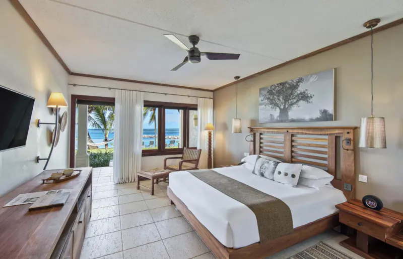 Luxury hotel bedroom with ocean view, king bed, ceiling fan, and balcony overlooking the beach