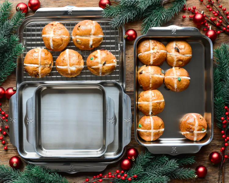 Hot cross buns on metal cooling rack and baking tray surrounded by Christmas greenery and red ornaments