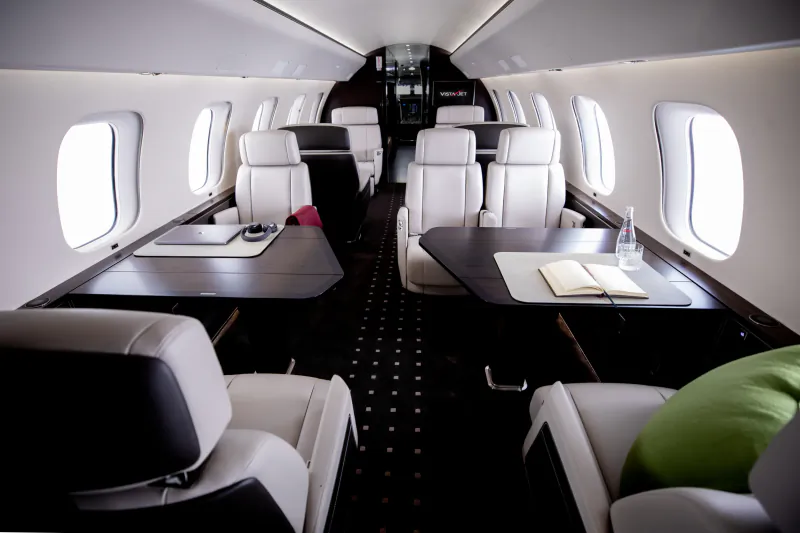 Luxury private jet cabin interior with white leather seats, dark wood tables, and large windows