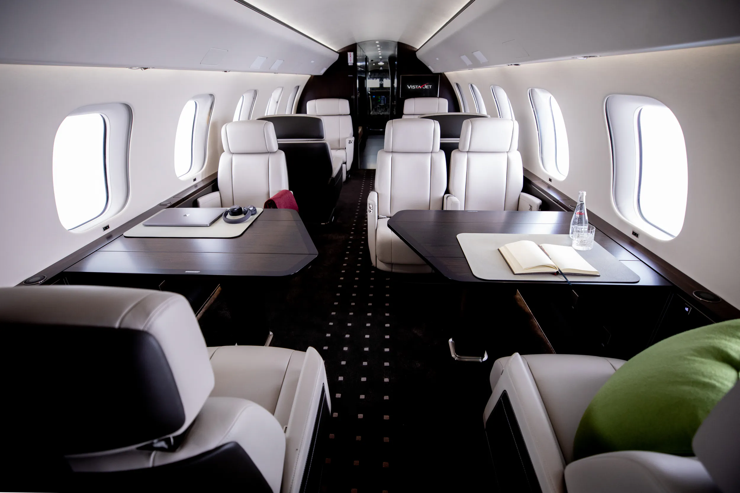 Luxury private jet cabin interior with white leather seats, dark wood tables, and large windows