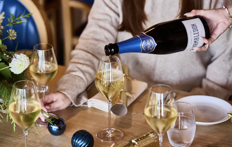 Woman pouring Ruinart champagne into a glass at a festive table with wine glasses and holiday decorations