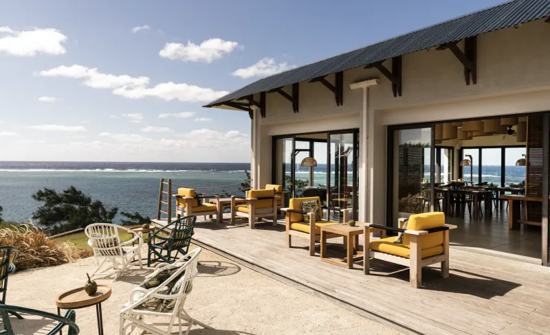 Luxury oceanfront terrace with yellow cushioned chairs and wooden tables overlooking the sea at Constance Tekoma, Rodrigues, Mauritius