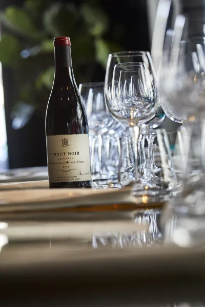 Bottle of Pinot Noir wine on a table with empty wine glasses and cutlery in the background