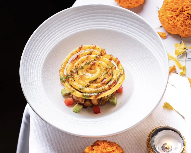 Elegant spiral of saffron-infused pasta on white plate with diced vegetables, garnished with edible flowers and spices
