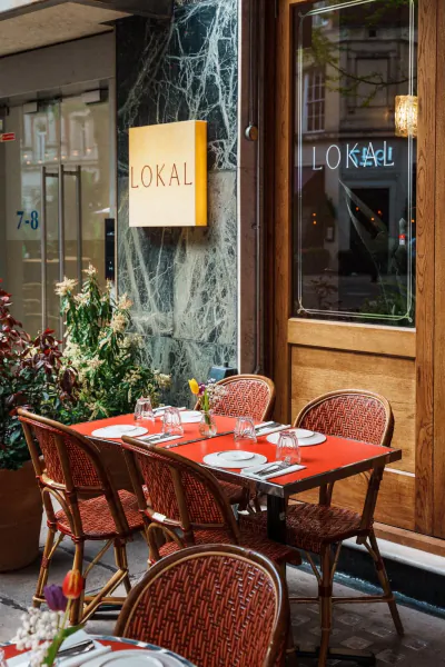 Outdoor dining area at Lokal restaurant with red tables, woven chairs, and Lokal signage on marble wall and window