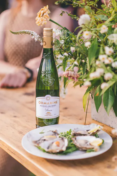 Bottle of Ormarine Picpoul de Pinet white wine beside a plate of fresh oysters with lemon on a wooden table