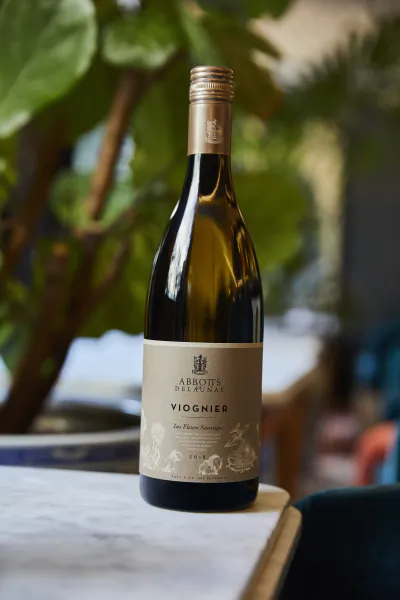 Bottle of Abbots & Delaunay Viognier white wine on a marble table with green foliage background