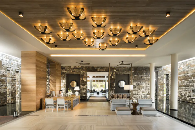 Luxury hotel lobby with stone walls, wooden ceiling, modern chandeliers, seating area, and reception desk