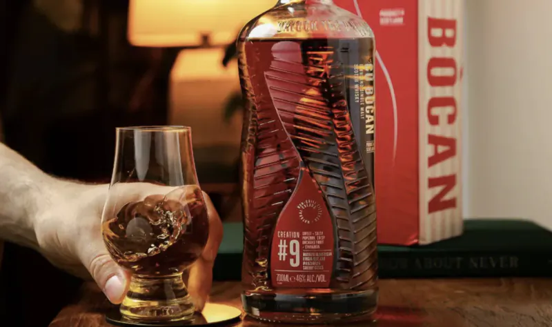 Hand holding a Glencairn glass of whiskey beside a bottle of The Macallan The Harmony Collection Rich Cacao single malt Scotch whisky