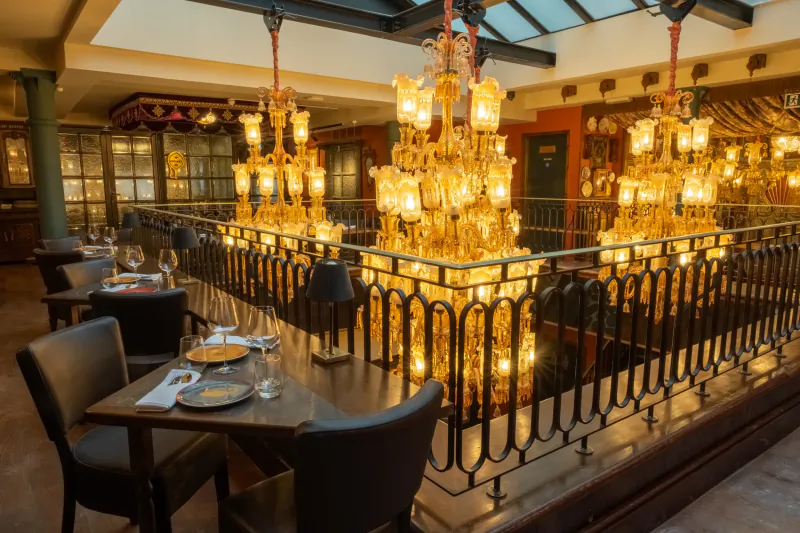 Elegant restaurant interior with ornate golden chandeliers above dining tables set with plates and glasses