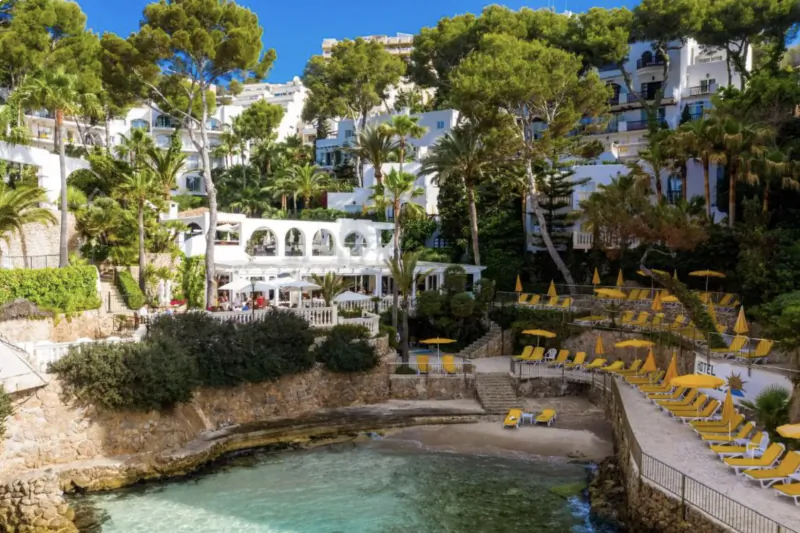 Clifftop resort with white buildings, yellow umbrellas, and a small cove with turquoise water