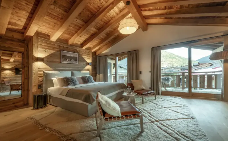 Luxury alpine bedroom with wooden beams, large bed, and mountain-view balcony in a chalet