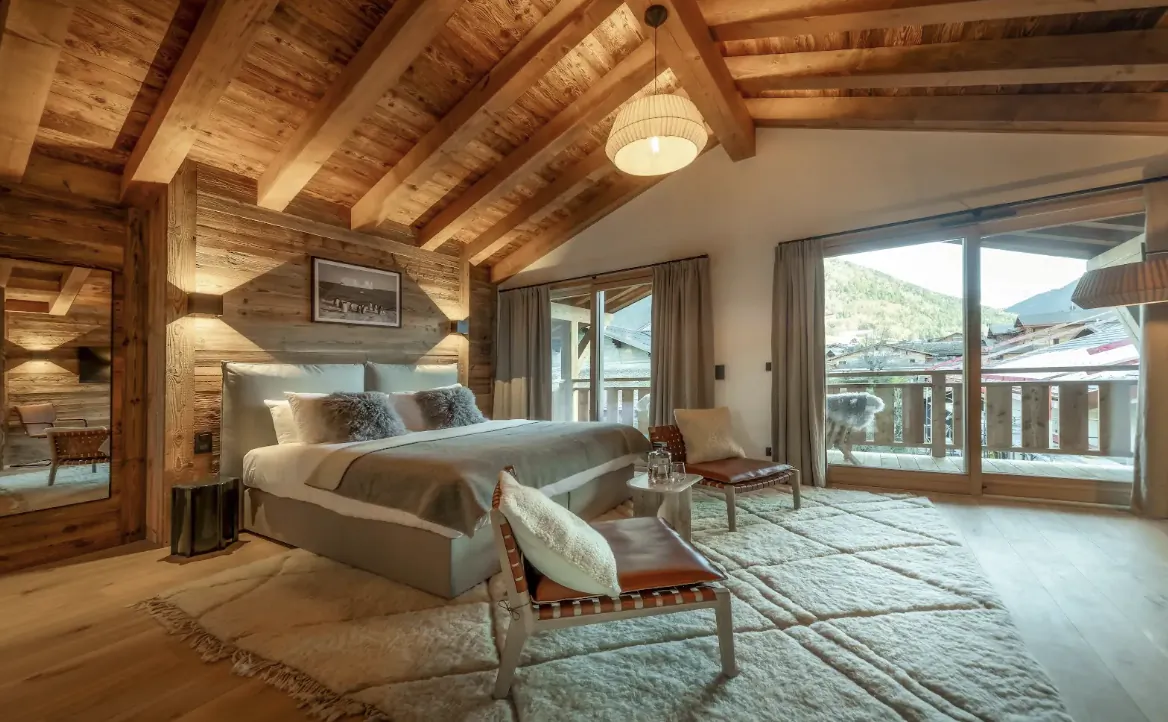 Luxury alpine bedroom with wooden beams, large bed, and mountain-view balcony in a chalet