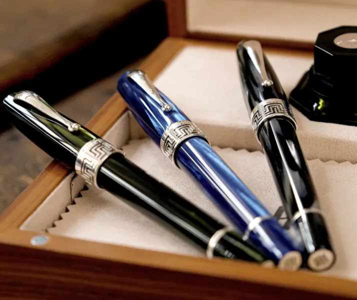 Three luxury fountain pens in a wooden presentation box: black, blue marbled, and black with silver Greek key bands
