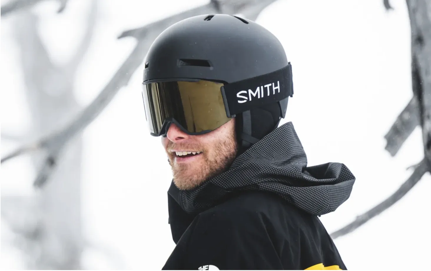 Smiling man in black ski helmet with Smith goggles and winter jacket outdoors in snow