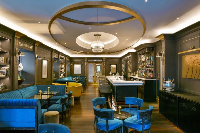 Elegant luxury hotel bar lounge with blue velvet seating, circular ceiling lights, and a long bar counter