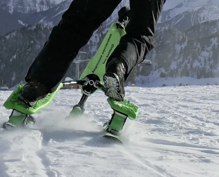 Person snowboarding on green Skki Trikke skis through deep powder with snow-covered mountains in background