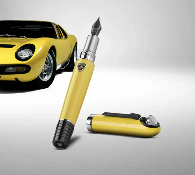 Yellow Lamborghini Miura sports car behind a yellow Montegrappa fountain pen with Lamborghini logo and matching yellow cap on white background