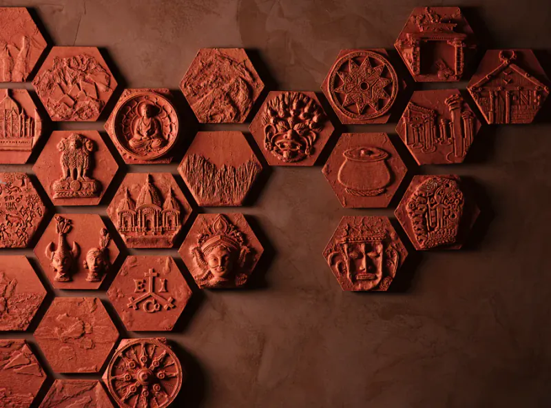 Hexagonal terracotta relief tiles depicting Indian cultural motifs including Buddha, Ashoka pillar, temple, and traditional symbols arranged on a wall