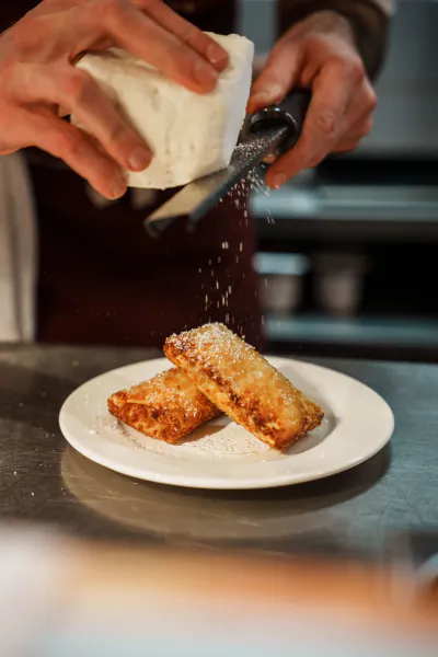 Chef grating white cheese over two golden-brown pastries on a white plate