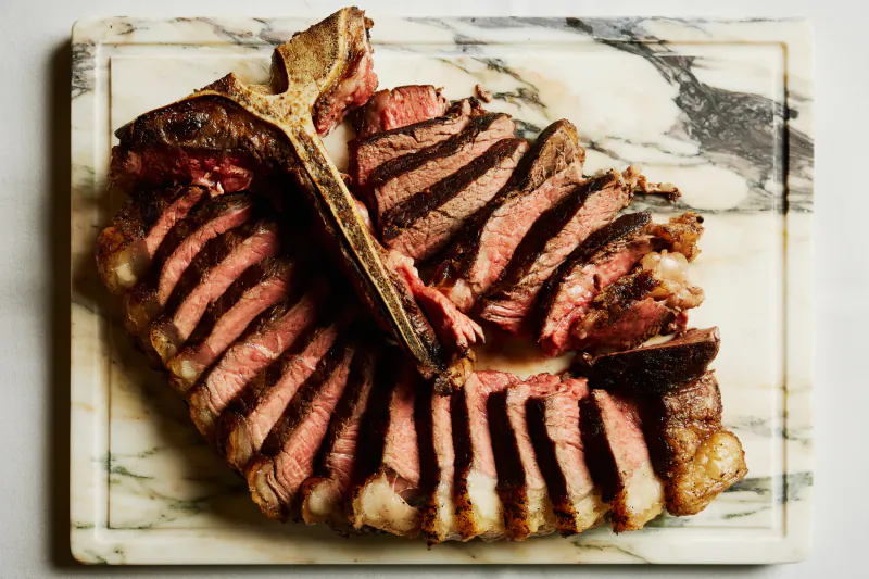 Sliced medium-rare T-bone steak with bone on marble cutting board