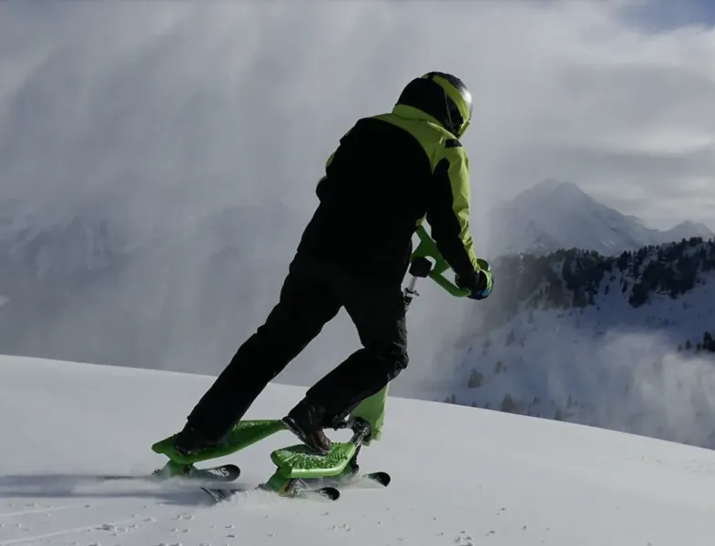 Person in neon green and black snow gear riding a green Trikke snow scooter down a snowy mountain slope