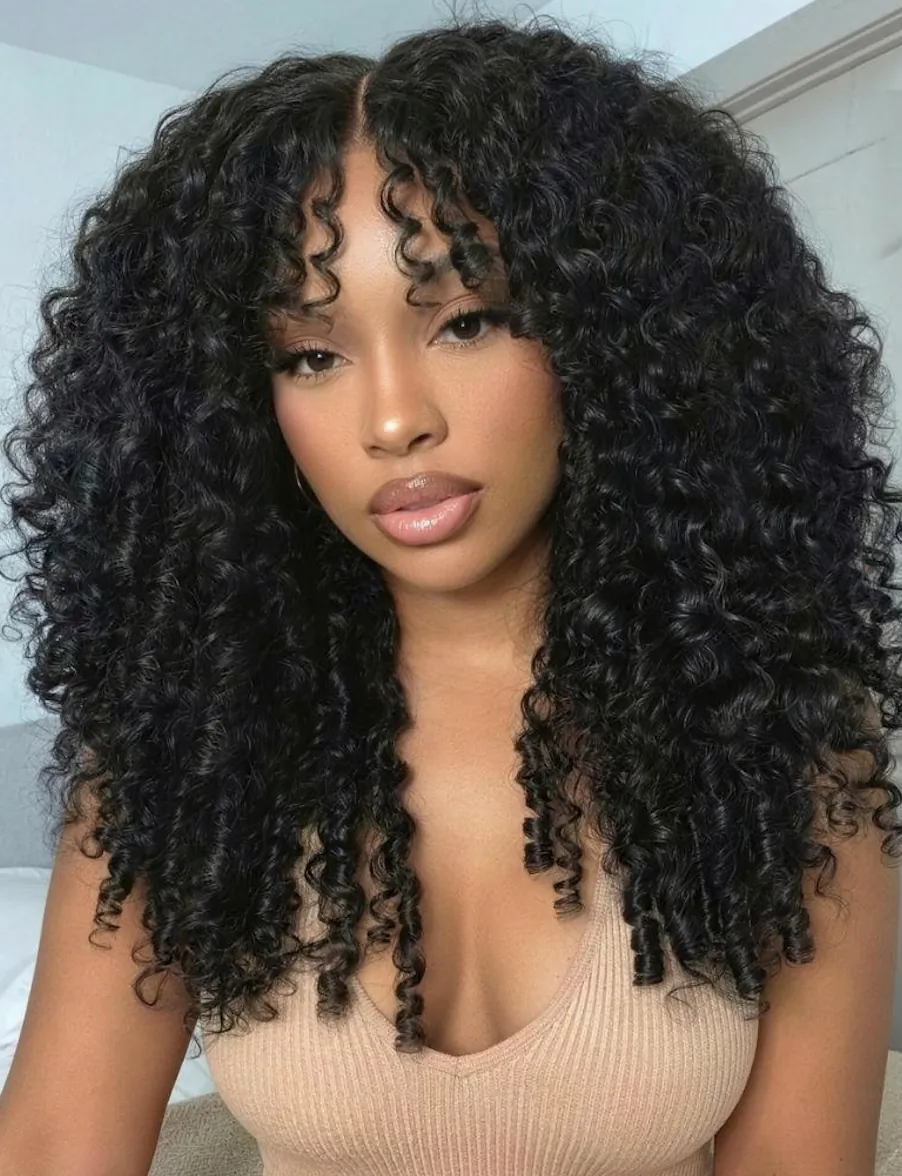 Woman with voluminous curly black wig, center part, wearing beige top