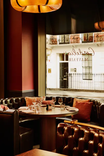 Cordelia’s Mayfair restaurant interior with tufted leather booths, round table set with wine glasses, and window view of the storefront