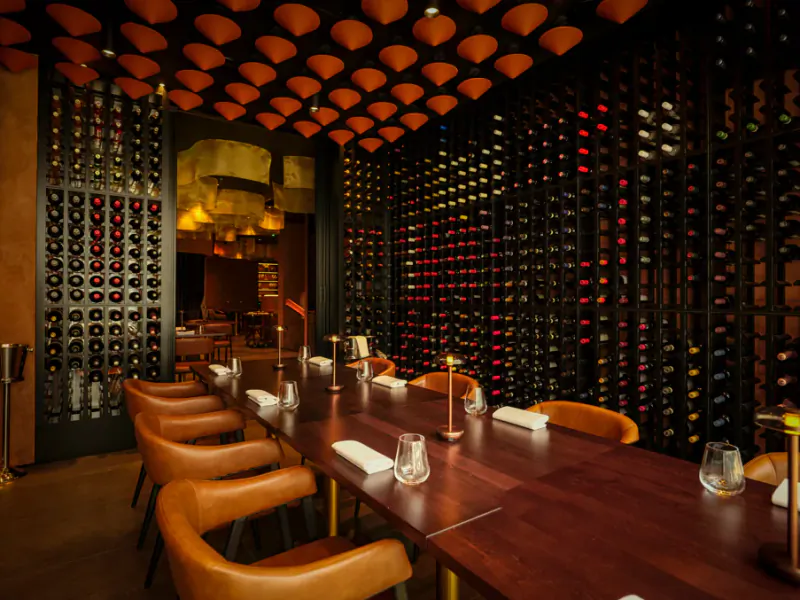 Elegant wine cellar dining room with long wooden table, brown leather chairs, and floor-to-ceiling illuminated wine bottle walls