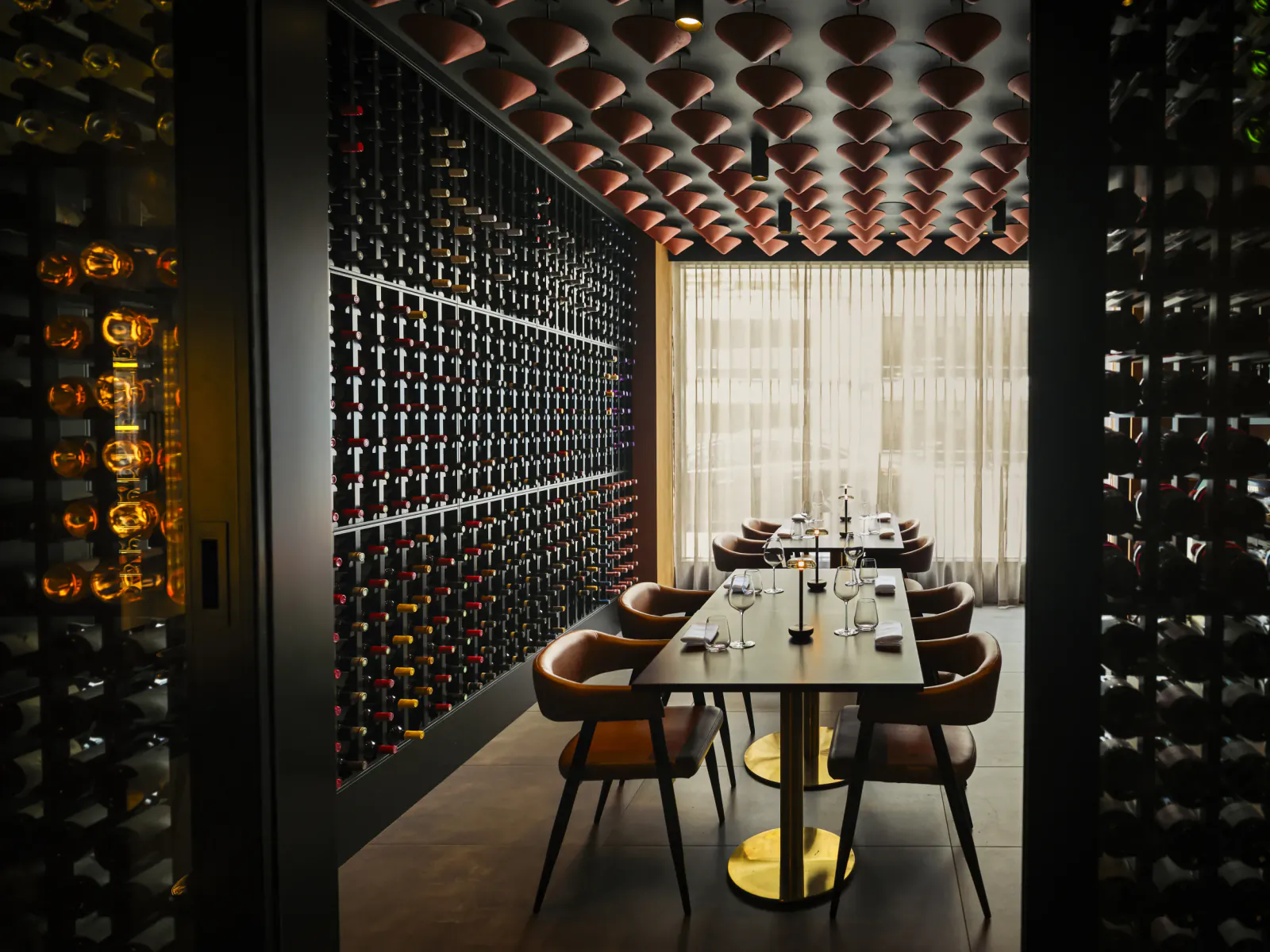 Elegant wine cellar dining room with long table, brown leather chairs, and floor-to-ceiling illuminated wine racks