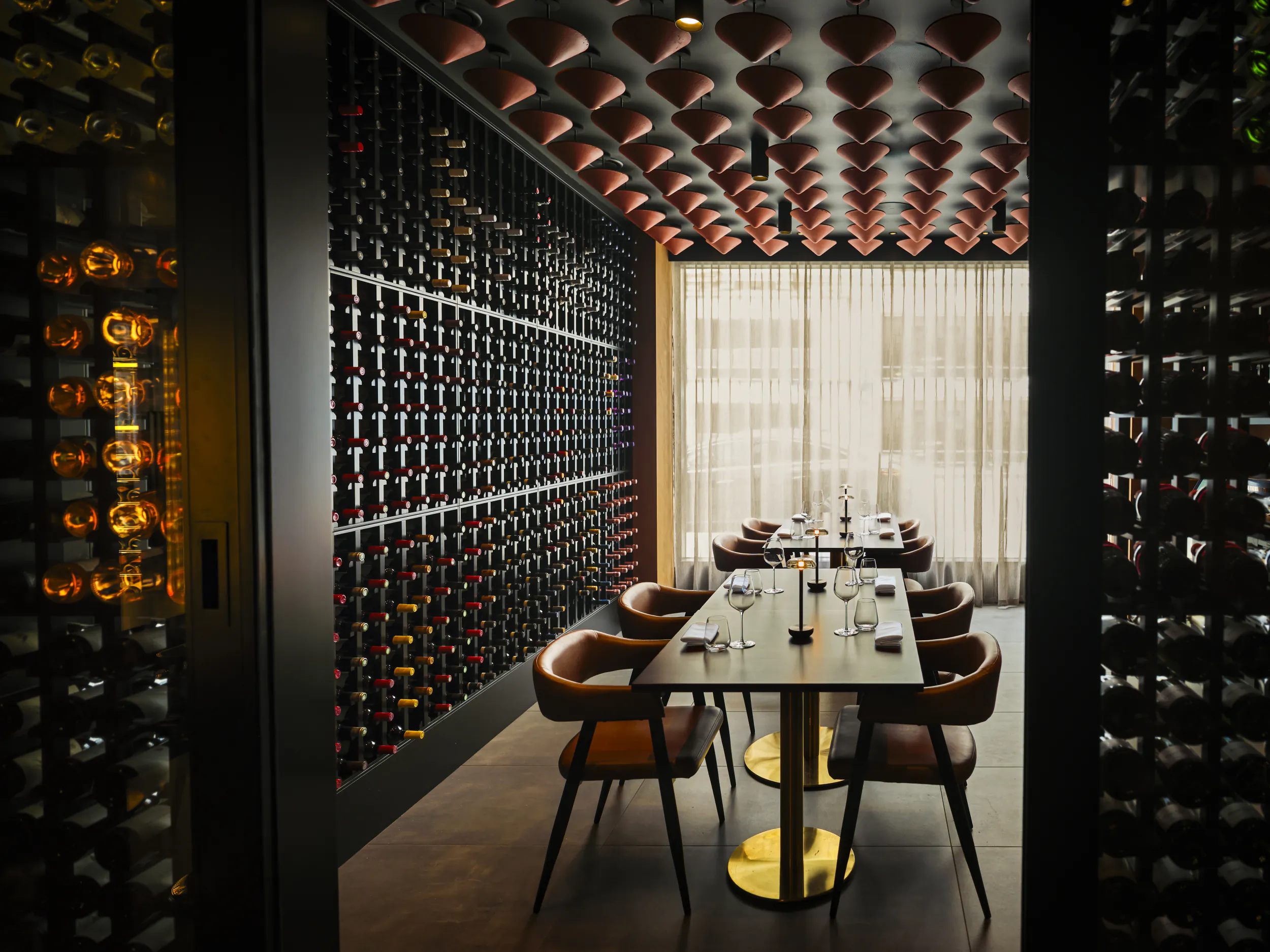 Elegant wine cellar dining room with long table, brown leather chairs, and floor-to-ceiling illuminated wine racks