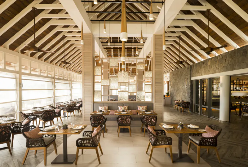Luxury hotel restaurant interior with high wooden ceiling, stone walls, and tables set with pink chairs overlooking large windows
