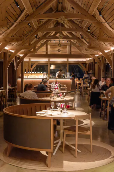 Elegant restaurant interior with exposed wooden beams, curved booth seating, and diners at tables in a warm, rustic setting