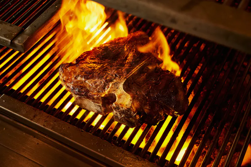 T-bone steak searing over open flames on a grill