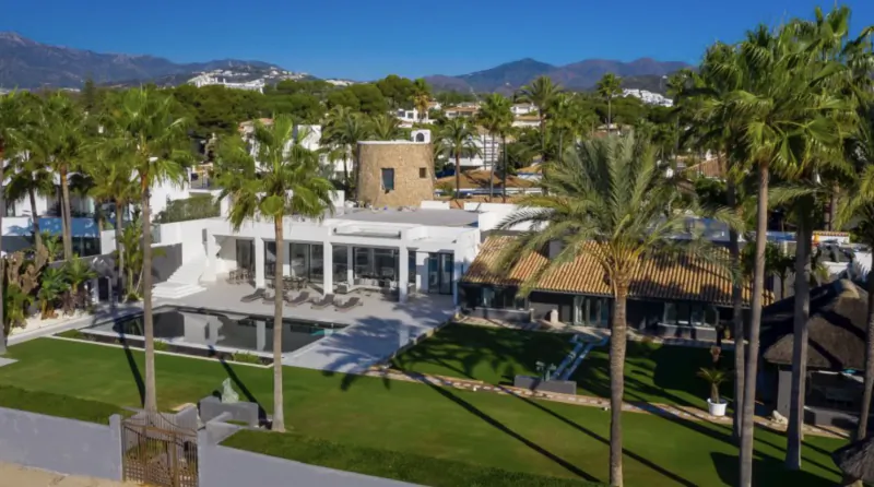 Aerial view of luxury villa Cilo Marbella with pool, lawn, and palm trees overlooking mountains
