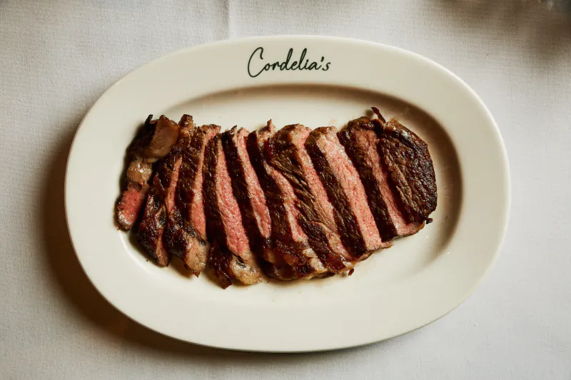 Sliced medium-rare steak on a white oval plate with Cordelia's logo