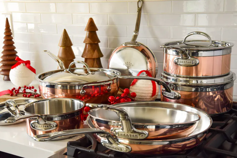 Assortment of copper and stainless steel pots, pans, and skillets on a stovetop with holiday decorations